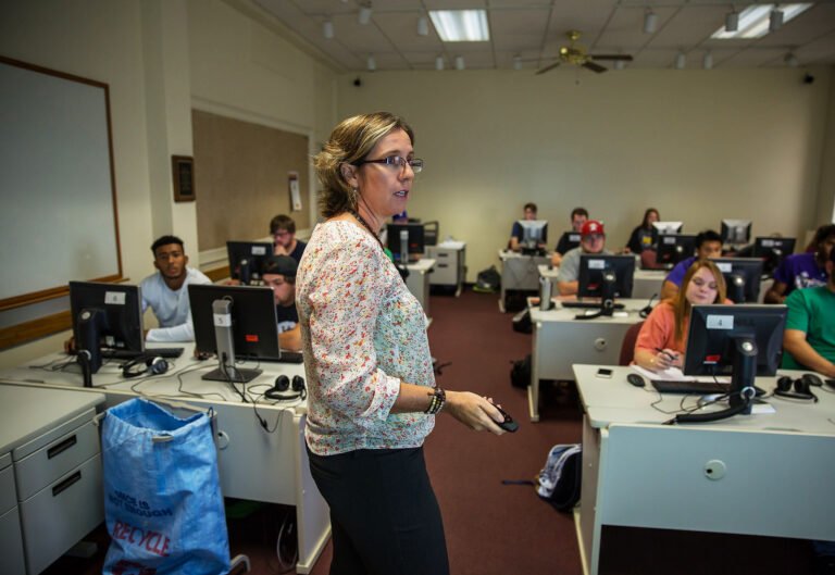 Kinesiology professor standing in front of class lecturing and pointing to white board