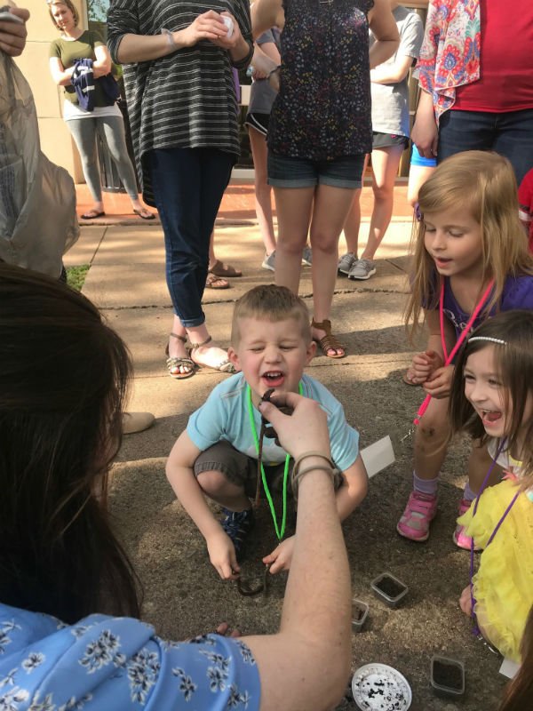 HSU student teacher holding up a dirt covered worm with young boy making silly face