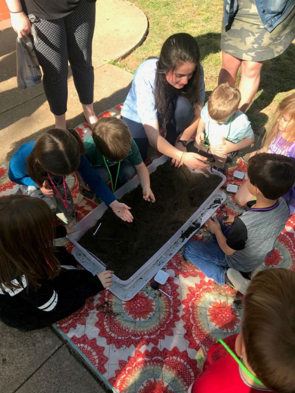 HSU student teacher and children playing in tub of dirt looking for worms