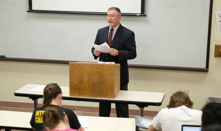 HSU professor standing behind a podium with a document in hand speaking to his students