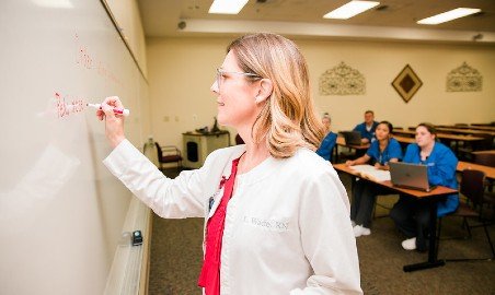 A nursing instructor writes on a whiteboard.