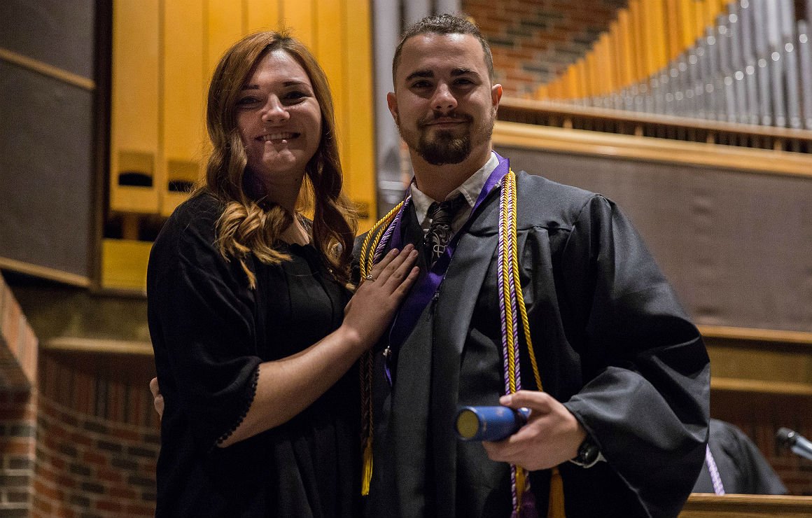 HSU graduate in graduation gown stands next to girl