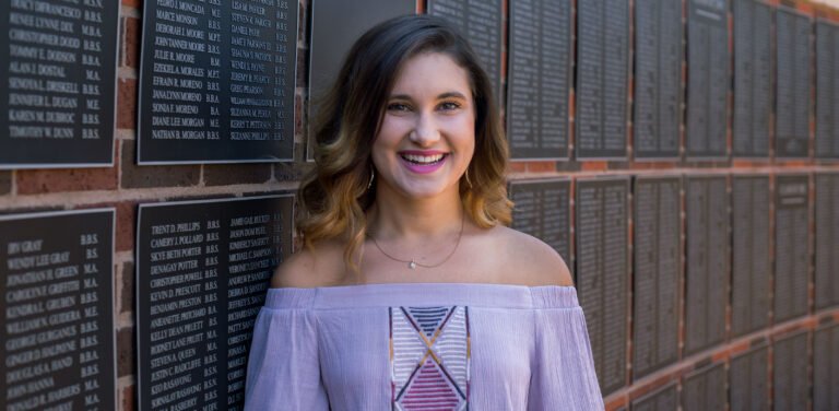 Photo of student with the alumni wall behind.