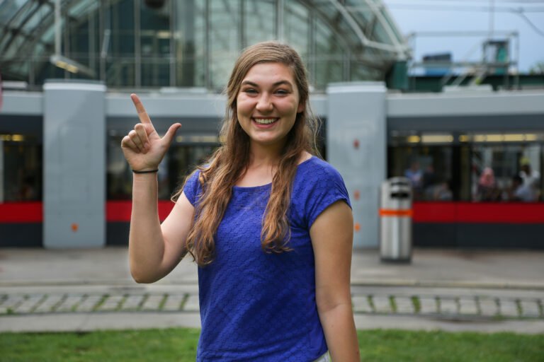 Photo of student showing cowboy sign while looking at the camera.