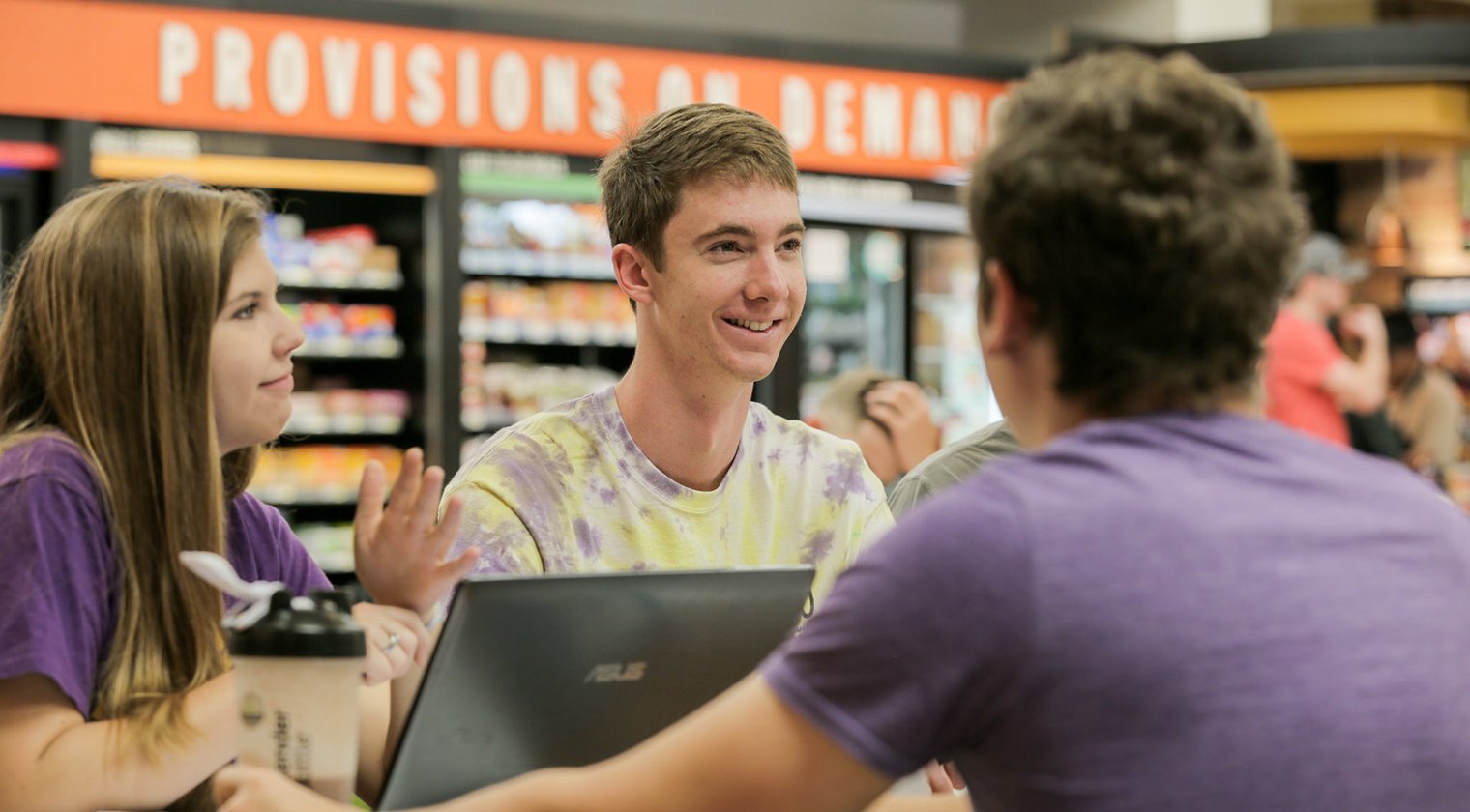 Photo of Three HSU students in focus enjoying conversation at the Moody Center POD.