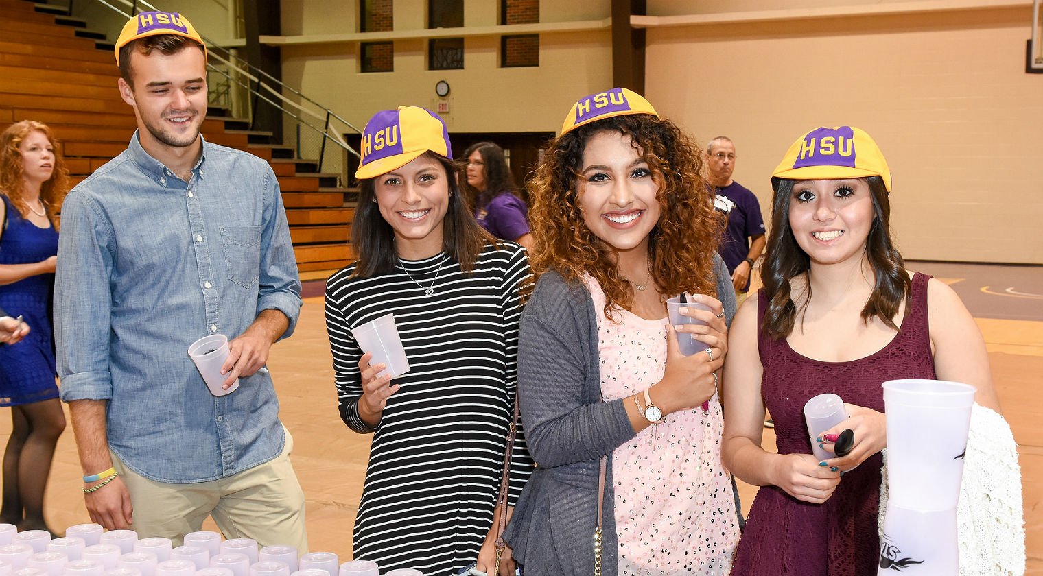 students standing next to table of refreshments wearing HSU hats