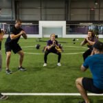 Students move into a squat position with the instructor of their workout course.