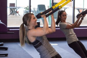 A student watches as an instructor models a move on the TRX straps in the fitness center.