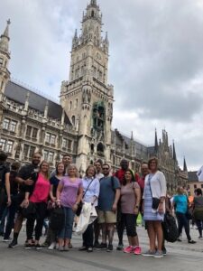 Two cohorts visiting Germany and Austria stand in front of the world famous Glockenspiel in the tower balcony of the Neues Rathaus in Marienplatz, Munich.