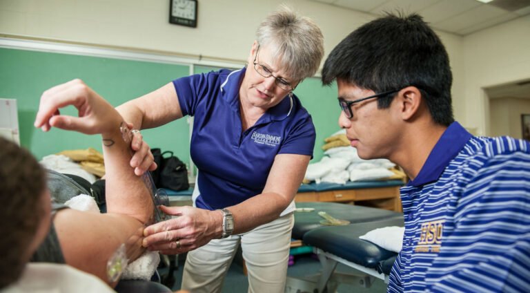 A physical therapy instructor shows a student how to treat an elbow injury