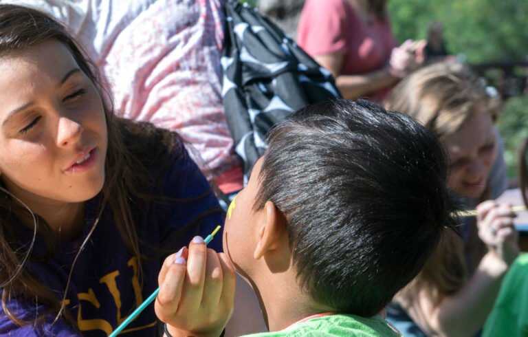 A Communication Sciences student paints a child's face at an event.