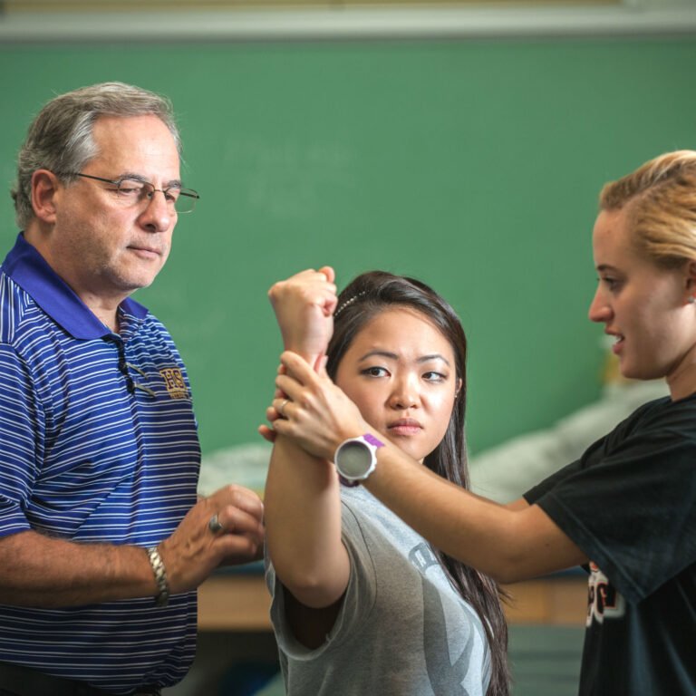 A student performs a physical therapy check while a professor observes.