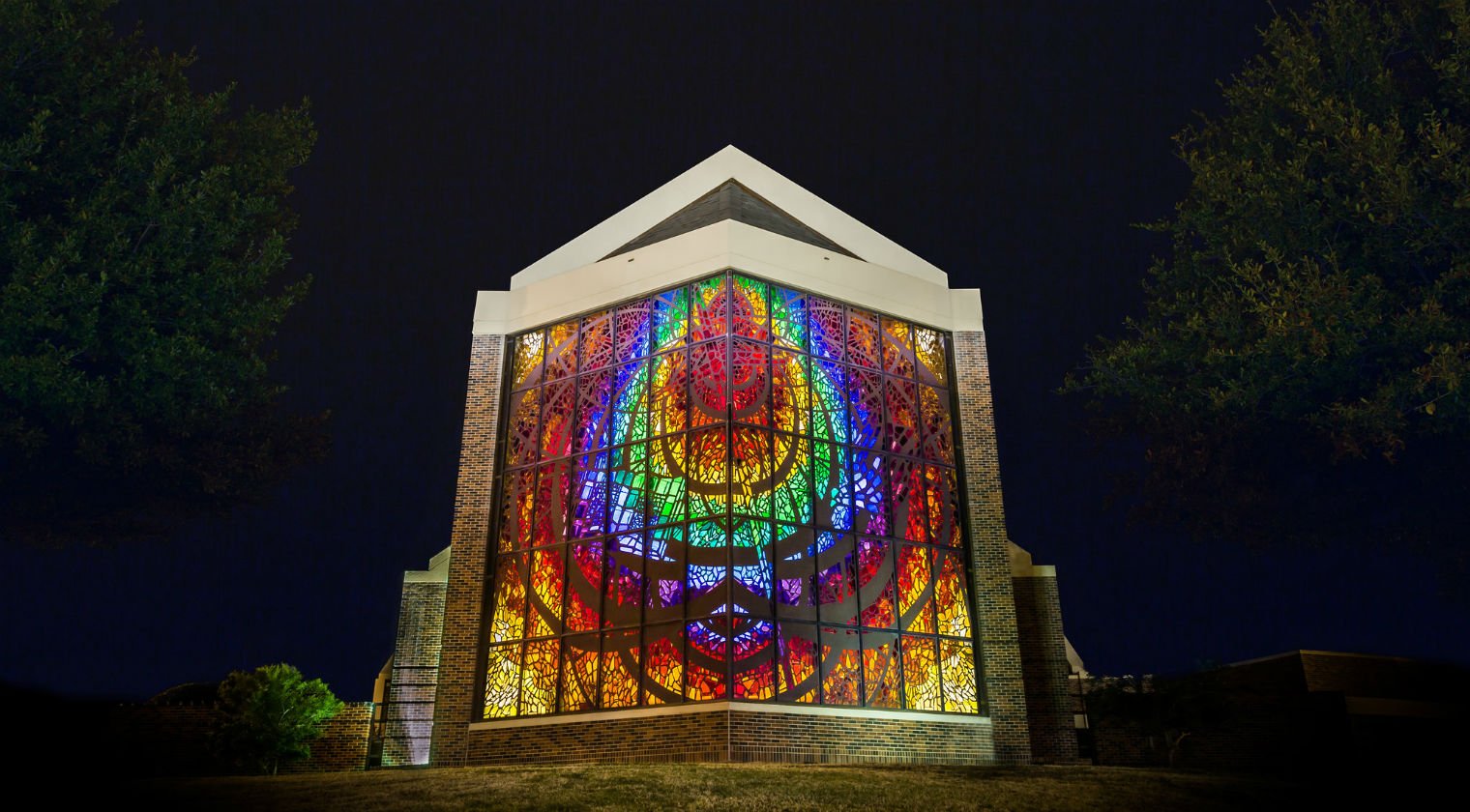 The Logsdon Chapel stained glass window shines brightly at night.