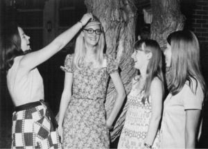 Several freshmen women laugh about how to properly wear a beanie at a lawn party thrown by Dr. and Mrs. Skiles in 1971.