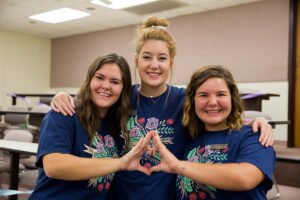 Members of Alpha Iota Omega show off their club sign at a homecoming event.