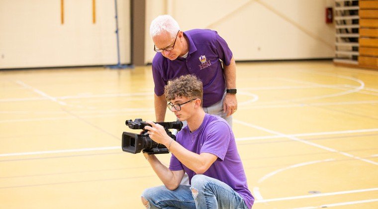 Staff member trains a student worker on camera operation.