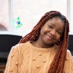 Student Charis Ochu smiles in an orange sweater.