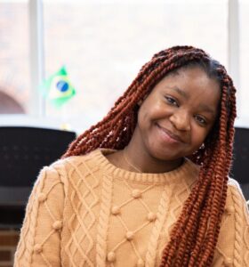 Student Charis Ochu smiles in an orange sweater.
