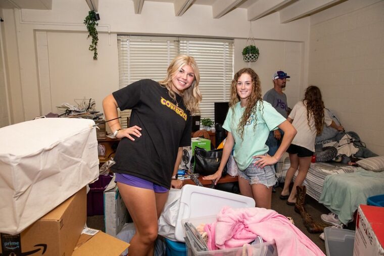 Roommates smile as they unpack their room.