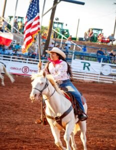 Kaylynn Reyna riding a horse a holding the American flag.