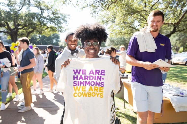 A student holds a t-shirt that says, "We Are Cowboys, We are Hardin-Simmons."