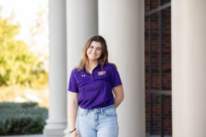 Student Esther Flowers stands in front of the Skiles Building in a purple shirt.
