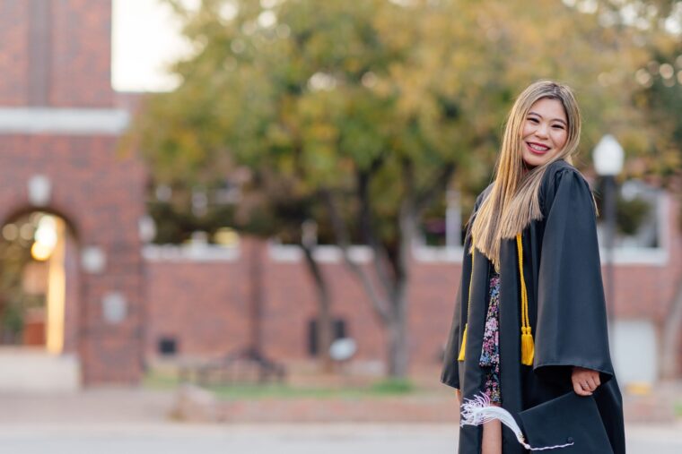 Emily Uhl in her graduation gown stands in front of the clock tower on campus.