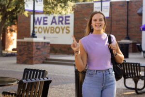 Sayler Beerwinkle in a purple shirt smiles on campus.