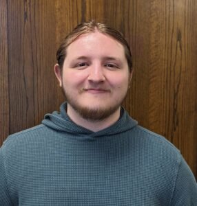 Student worker Mason A Duebner stands in front of a door.