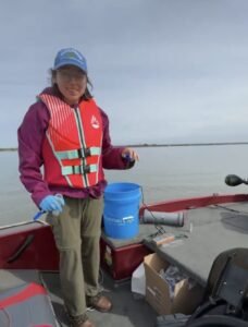 Maya Morell in a boat posing with a sample of local lake water.
