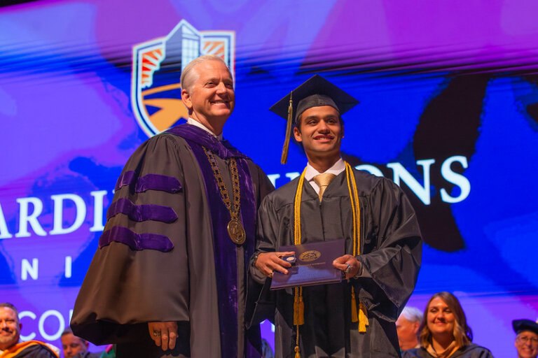 President Bruntmyer smiling on stage with a student at graduation.