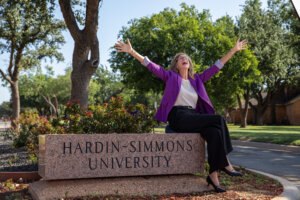 VP of Advancement sitting on an HSU sign with her hands up in joy- celebrating the end of a great campaign