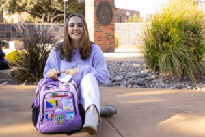 Student sitting in the alumni wall with backpack
